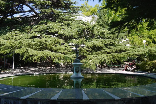 Friluftsområde med en stor fontän med en sten skulptur i centrum mot bakgrund av grön barrträd — Stockfoto