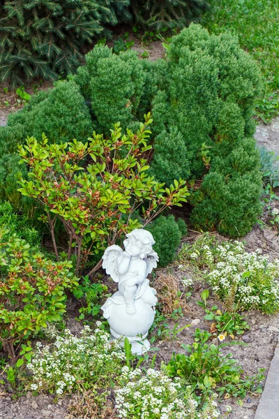 小天使的雕塑在公园附近的绿色灌木和花朵的下巴休息. — 图库照片