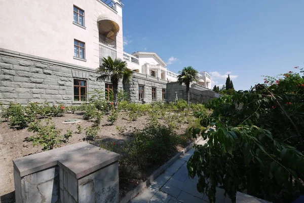 Palmeras que crecen entre flores en un macizo de flores junto a un edificio de hermosa arquitectura — Foto de Stock