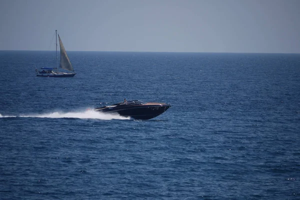 Un poderoso barco con turistas diseccionando las aguas del mar azul y un velero flotando cerca . — Foto de Stock