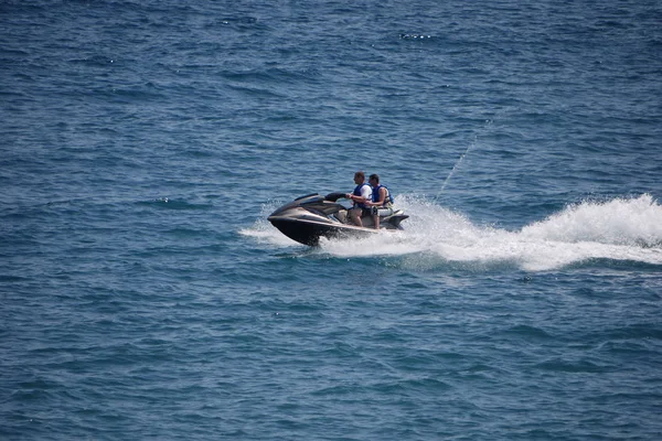 Los turistas viajan a gran velocidad en una motocicleta acuática en medio de las tranquilas aguas del mar. Vestido para la seguridad en chalecos salvavidas . — Foto de Stock