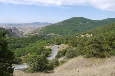 Kayalık dağ zirveleri yeşil büyümüş orman ve bunlar arasında çalışan yol ile mahallede
