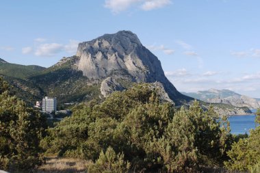 Deniz kıyısına yakın kayaları olan dağlar. Sahilde yeşillik ler ve birkaç ev var.