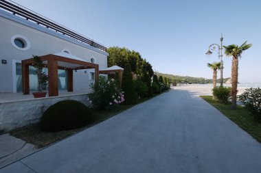 Mavi denize karşı yanlarda dekoratif bitkiler, palmiye ağaçları ve restoranlar ile bir gezinti
