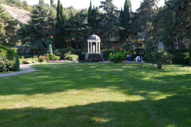 Kırpılmış çalıların parlak renkleri ile yeşil bir çim ve sütunlar ve kubbeli çatılı bir kule ayakta beyaz heykeli ile güzel bir park.