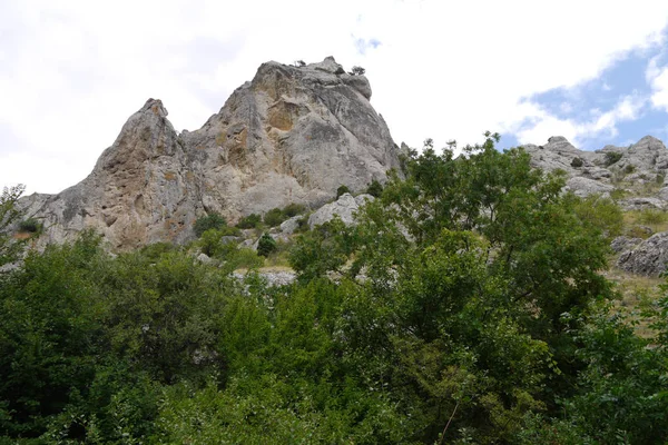 Pico de montanha íngreme rochoso contra um fundo de árvores decíduas baixas — Fotografia de Stock