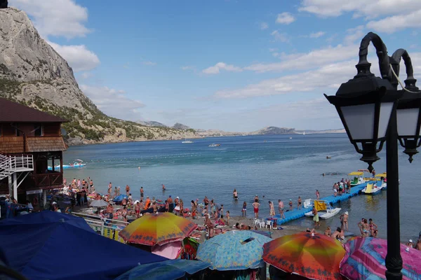 Μια παραλία γεμάτη από τουρίστες και τις πολύχρωμες ομπρέλες από την ακτή της θάλασσας στο βάθος ενός ψηλού βουνού βραχώδη — Φωτογραφία Αρχείου