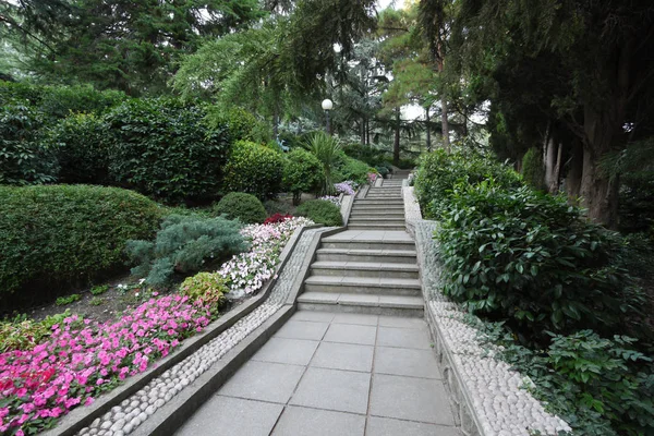 Po schodach w parku na tle kwiatów i krzewów — Zdjęcie stockowe