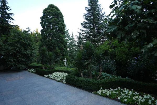 Сад с деревьями, пальмами, цветами и кустами, в котором стоит белая статуя человека — стоковое фото