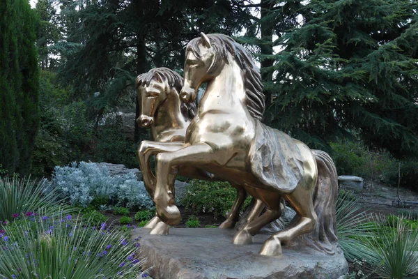 Un pedestal que representa dos caballos lisos dorados, sobre un fondo de una zona verde del parque — Foto de Stock