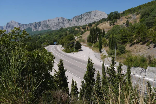 La route est tordue sur le fond des falaises escarpées entourées par une forêt dense — Photo