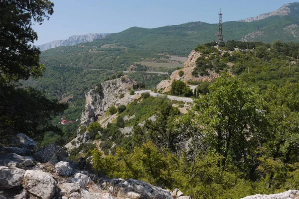 Torto strada rocciosa sullo sfondo di alte montagne coperte di alberi — Foto Stock