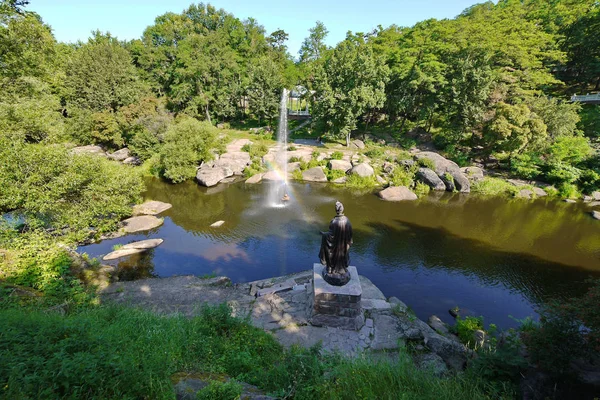 Schöner Brunnen inmitten eines breiten felsigen Flusses vor dem Hintergrund dicht grüner Bäume — Stockfoto