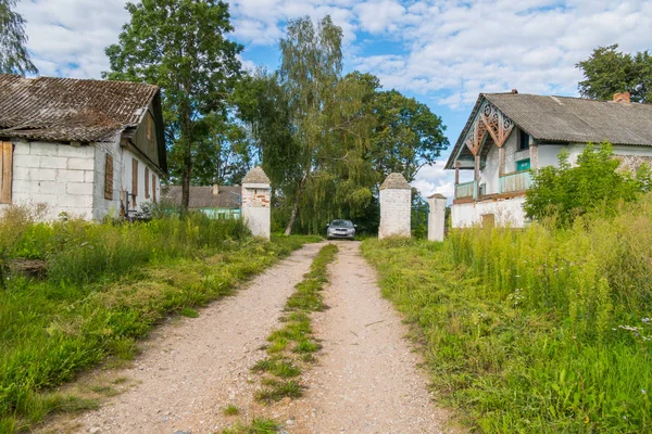 Długie szerokie drogi jest otoczony trawą na tle opuszczonych domów i wysoki, bujnych drzew — Zdjęcie stockowe