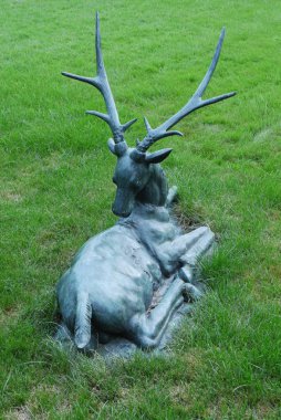 Yeşil çim üzerinde büyük dallı boynuzları olan bir geyik teneke heykeli