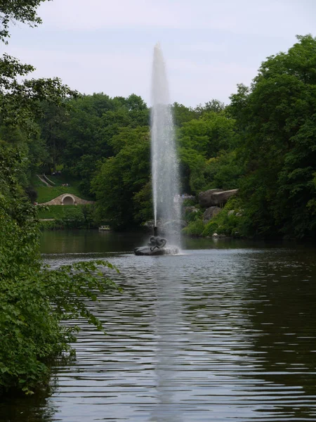 En stor fontän mitt i sjön mot bakgrund av vackra välskötta gräsmattor och gröna träd — Stockfoto
