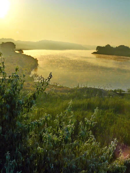 Uma bela imagem do nascer do sol sobre o rio com margens pitorescas com grama verde e árvores envoltas em névoa matinal . — Fotografia de Stock