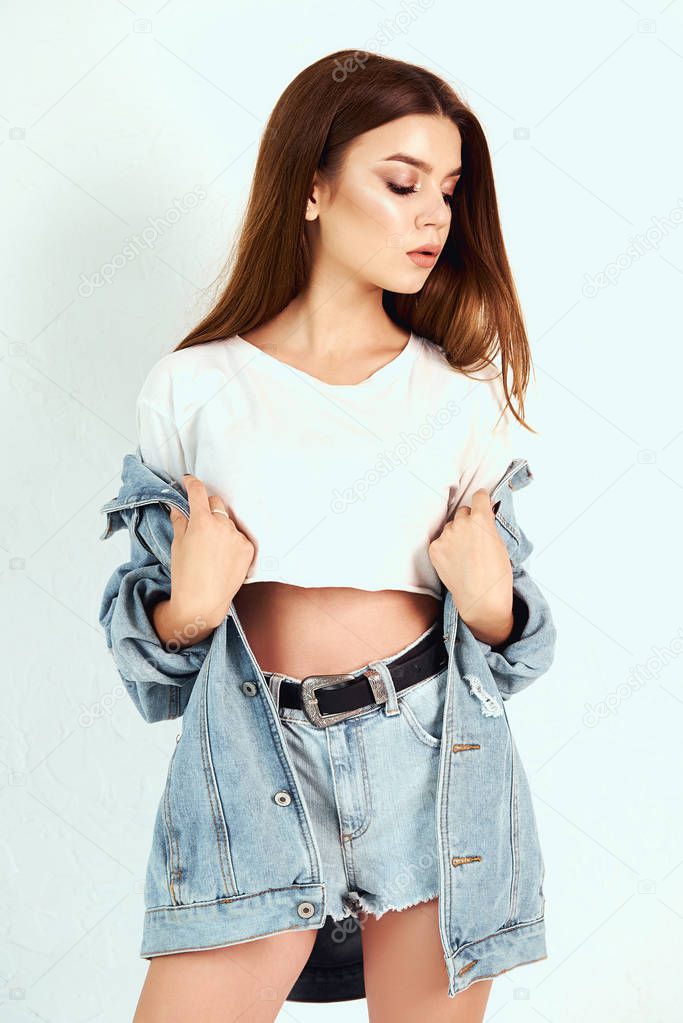 A girl in a denim jacket and short shorts. Posing in the studio on a white background