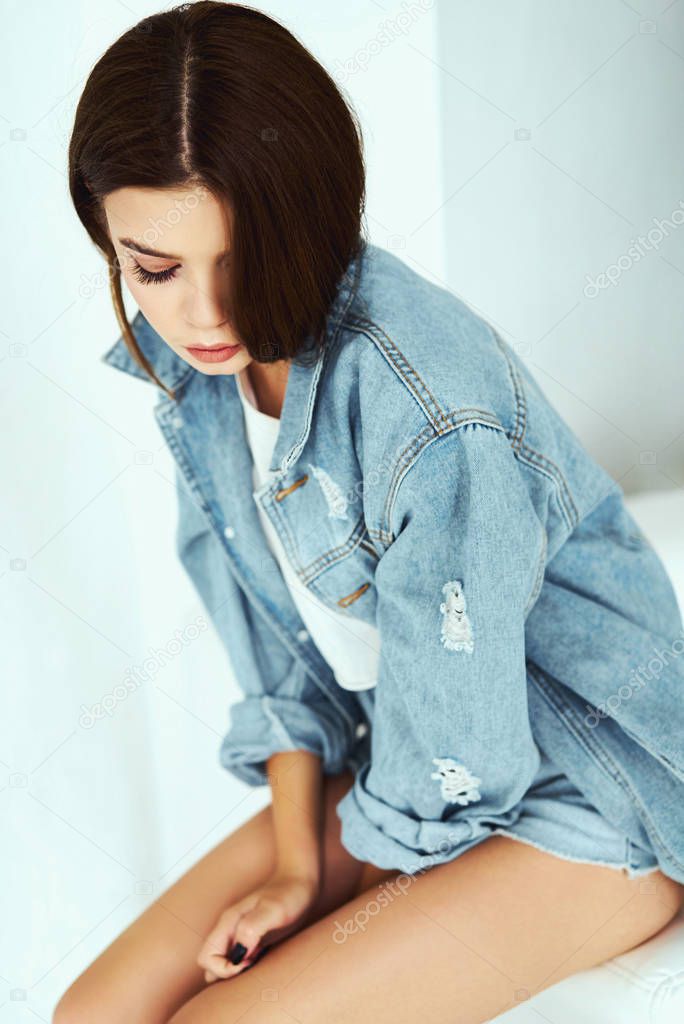 A girl in a denim jacket and short shorts. Posing in the studio on a white background