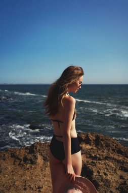 Gülümseyen ve tropik ada sahilde yalan hayattan zevk. Şık bikini, güneş gözlüğü ve geniş şapka giyiyor. Genç ve güzel bronzlaşmış modeli yaz yaşam tarzı portresi.