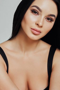 Stüdyoda poz veren koyu saçlı güzel bir kadın. Doğal ışık ile beyaz bir arka plan üzerinde Portre. Saf elbise, topuklu ayakkabı, makyaj