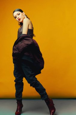 Kırmızı arka planda şık kıyafetler içinde poz veren genç ve güzel bir manken. Moda, şık kıyafetler, aksesuarlar, güzellik