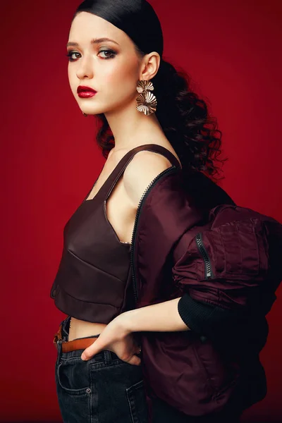 Joven modelo hermoso posando en ropa elegante sobre un fondo rojo. Moda, ropa elegante, accesorios, belleza — Foto de Stock