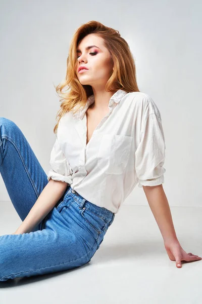 Estilo de ropa urbana minimalista, maqueta para la tienda de impresión de camisetas. Chica vestida en blanco camiseta blanca y jeans posando contra la pared blanca — Foto de Stock