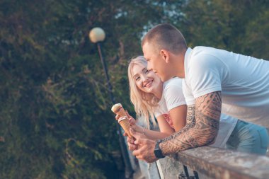 Sarışın kız ve bir adam dondurma ile ayakta ve Park arka plan ağaç üzerinde gülümseyen