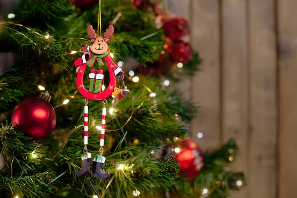 Christmas deer toy on a branch of a Christmas tree with a garland and red balls on a wooden wall background