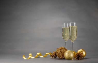 İki bardak şampanya Noel oyuncaklar ve gri arka plan üzerinde altın bir kurdele ile süslenmiş
