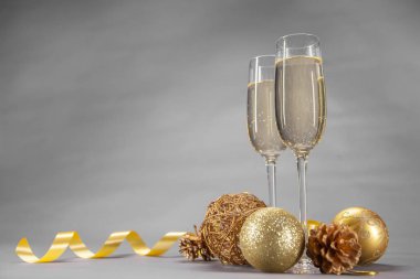 İki bardak şampanya Noel oyuncaklar ve gri arka plan üzerinde altın bir kurdele ile süslenmiş
