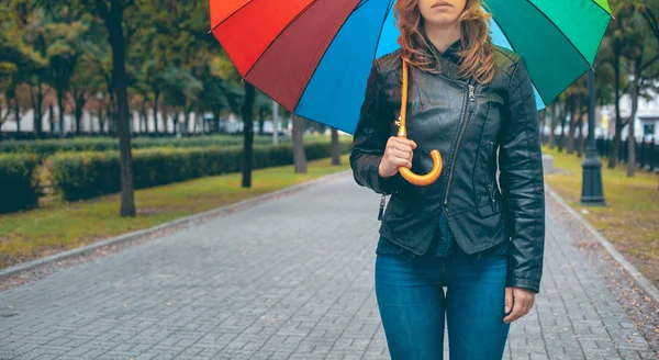 girl in a black leather jacket and blue jeans with a multi-colored umbrella in her hands on the mall