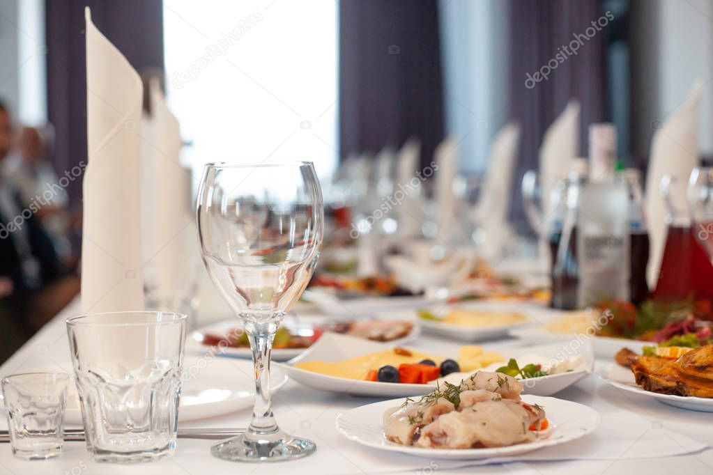 The served festive table is covered with a white tablecloth with dishes and drinks with glasses in the ceremonial hall