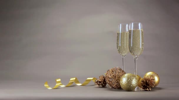 两杯香槟酒的气泡上升是金色的圣诞玩具之一 上面有一条灰色背景的丝带 — 图库视频影像