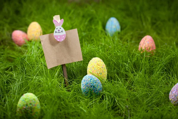 Colored Easter eggs in the grass next to Kraft paper topper decorated with an Easter bunny with space for text