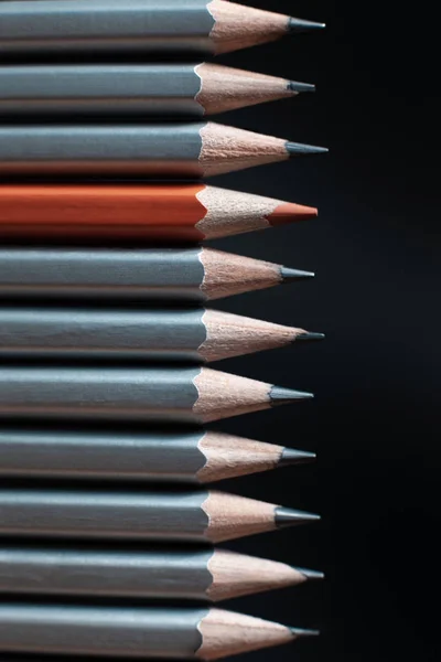 Red sharpened pencil between gray pencils isolated on black background