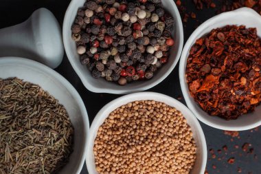 Paprika, hardal, kestane tohumu ve siyah arka planda izole edilmiş havan topunun yanında beyaz seramik kaselerde biber karışımı.