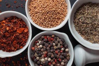 Paprika, hardal, kestane tohumu ve siyah arka planda izole edilmiş havan topunun yanında beyaz seramik kaselerde biber karışımı.