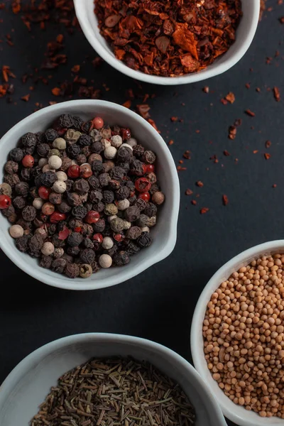 Paprika, hardal, kestane tohumu ve siyah arka planda izole edilmiş havan topunun yanında beyaz seramik kaselerde biber karışımı.