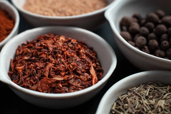 Paprika, hardal, kestane tohumu ve siyah arka planda izole edilmiş havan topunun yanında beyaz seramik kaselerde biber karışımı.