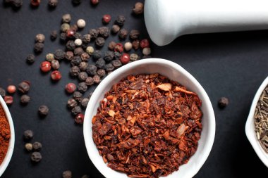 Paprika baharatı seramik bir kasede bezelyelerin yanında seramik bir havan topunda biberli mısır ve karanfil tohumlarıyla saçılmış.