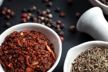 Paprika baharatı seramik bir kasede bezelyelerin yanında seramik bir havan topunda biberli mısır ve karanfil tohumlarıyla saçılmış.