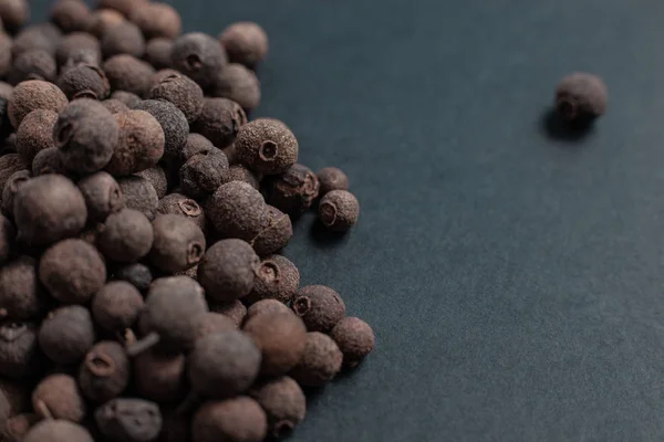 Spice allspice black peppercorns scattered on a black background