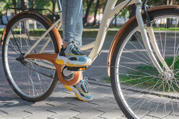明るいスニーカーの足の靴はベージュの自転車のペダルの上に立つ — ストック写真
