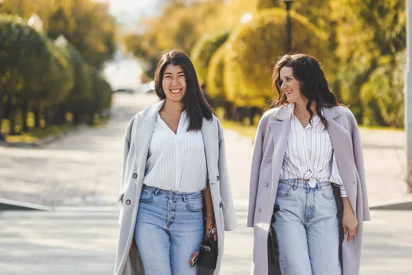 Neşeli iki kız arkadaş şehrin yaya geçidinde karşıdan karşıya geçerken kucaklaşırken eğleniyorlar.