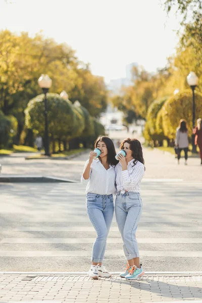 Neşeli iki kız arkadaş şehrin yaya geçidinde karşıdan karşıya geçerken kucaklaşırken eğleniyorlar.