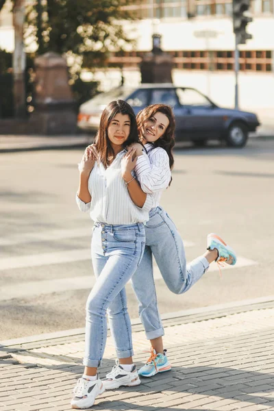 Neşeli iki kız arkadaş şehrin yaya geçidinde karşıdan karşıya geçerken kucaklaşırken eğleniyorlar.