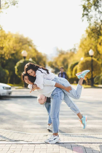 Neşeli iki kız arkadaş şehrin yaya geçidinde karşıdan karşıya geçerken kucaklaşırken eğleniyorlar.