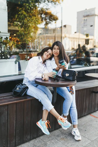 Gülümseyen neşeli kadın arkadaşlar kahve içiyorlar telefonla kameraya bakıyorlar caddedeki kafede oturuyorlar.